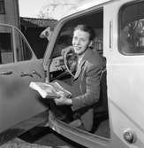 Arboga Tidning, personal.
Willy Johansson sitter bakom ratten. Han har en bunt tidningar i handen.
Interiör av bil, instrumentbrädan syns delvis.