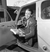 Arboga Tidning, personal.
Willy Johansson sitter bakom ratten. Han har en bunt tidningar i handen.
Interiör av bil, instrumentbrädan syns delvis.