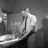 Arboga Tidning, personal och interiör. En man, med uppkavlade skjortärmar, packar tidningar. Tidningsbuntar ligger i travar. Ytterdörren står öppen.