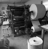 Arboga Tidning, interiör.
Tryckpress med två stora pappersbalar monterade. En stor, färdigtryckt, pappersrulle står på golvet.