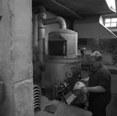 Arboga Tidning, personal och interiör. En man, iklädd overall, arbetar vid en maskin. Han håller i en plåt som används för att trycka en tidningssida. Flera plåtar syns till vänster i bild. Mannen vistas i en källarlokal.