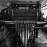 Arboga Tidning, interiör. Tryckpress i arbete. Tidningspapperet rusar över valsarna. En soptunna syns i förgrunden och ett fönster syns i bakgrunden.