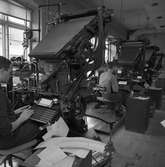 Arboga Tidning, personal och interiör. Fyra sättningsmaskiner står uppställda intill fönstren. Varje maskin har ett tangentbord och två män ses skriva på dem.