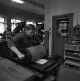 Arboga Tidning, personal och interiör. En man med en vals. I bakgrunden syns flera maskiner, en arbetsbänk och en dörr till ett annat rum.