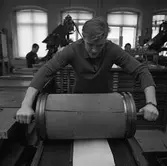 Arboga Tidning, personal och interiör. En man med en tygklädd vals. I bakgrunden syns två män vid var sin maskin.