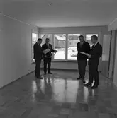 Arbogavillan lll, interiör. På parkettgolvet, i det tomma vardagsrummet, står fyra herrar och diskuterar. De håller i papper, möjligen ritningar. 
Hildning Lund, från Byggnadsfirma Lund, är nummer två från vänster.
Nummer tre, från vänster, är Norberg. Han är verkmästare hos Lund.
Nummer fyra, är Hilding Karnéus, från Arboga Sparbank.