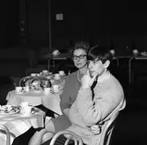 Arbogabor deltar vid radioprogrammet Frukostklubben, ett underhållningsprogram som sänds på lördagsmorgnar. En kvinna och en ung man sitter vid ett runt bord och dricker kaffe.