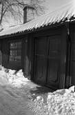 Del av ett boningshus på Ahllöfsgatan. Huset har dubbeldörr och spröjsat fönster. Snön ligger på taket och det är snödrivor på var sida om porten. Porten har ett handtag och en stor nyckel i låset.
Enligt skylten vid dörren är gatnumret 13.