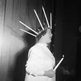 Arbogarevyn spelar upp sin Jubileumsrevy. Man utklädd till Lucia med långa stearinljus i kronan och ett ljus i handen.