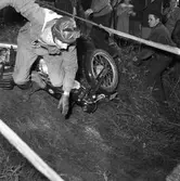 Arbogas Stjärnknutte
Tävling i terrängkörning med motorcykel. En man har kört omkull. Han har vindglasögonen i pannan. Publiken står alldeles intill i backen.