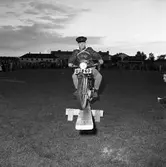 Arbogas Stjärnknutte
Tävling. Man som balanserar med motorcykel på bräda
Platsen är en fotbollsplan och en stor publik ser på.