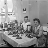 Börjesson tillverkar Arbogaspegel
Ett par sitter vid köksbordet. De har spegelramar uppställda på bordet. Kvinnan har förkläde på sig. På väggen hänger en almanacka. Genom fönstret syns villor.