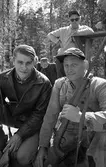 AT-skytte
Två män, den vänstra är Bernt Andersson från Götlunda. Mannen med geväret är oidentifierad. Flera personer syns i bakgrunden. De befinner sig i skogen.
(AT kan betyda Arboga Tidning)
