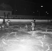 Bandy. Det ena laget är Lions Clubs lag Flying Lions. Okänt vilka de spelar mot. Matchen spelas utomhus inför en stor publik.
Alternativa sökord: Rinkbandy, hockeybockey