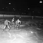 Bandy. Det ena laget är Lions Clubs lag Flying Lions. Det andra laget är okänt. Matchen spelas utomhus inför en stor publik.
Alternativa sökord: ringbandy, hockeybockey