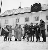 Barn med julklappar. En flicka har fått en docka. Två flickor i nya kläder. En pojke med en minicykel. Två barn har fått armbandsklockor. Fickan längst till höger håller en hund i famnen.