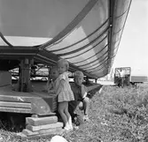 Barnens Dag. Tre barn står under något som kan vara en åkattraktion. Den står inte på någon festplats. En man, med bar överkropp, kommer gående mot dem.