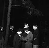 Belöning till scouter.
En kvinna fäster något på rockslaget på en annan kvinna. Tre herrar i slips och kostym tittar på, den tredje från vänster är Harald 