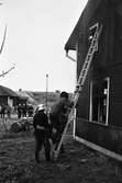 Brandövning vid Sverkesta. Brandsoldater med uniformer och hjälmar. En person klättrar nerför en stege från andra våningen på huset.