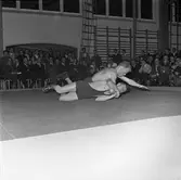 Tävlingen Fyrstadsbrottning. Deltagande städer: Arboga, Eslöv, Uddevalla och Falkenberg.
Två män på mattan. Publik i gymnastiksalen.
Arboga Atletklubb