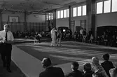 Brottning för ungdomar. Två matcher pågår samtidigt i gymnasikhallen. En segrare koras. Publiken sitter efter väggarna.
1960-talet