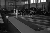 Brottartävling, för ungdomar, i en gymnastiksal. Publiken sitter efter väggarna. Det pågår två brottningsmatcher samtidigt.