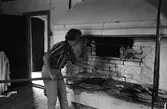 Brödbakning vid Jäders bruk. En kvinna i en bakstuga/bagarbod. Hon håller i en brödspade med knäckebröd. Vid det ena fönstret finns ett bakbord med brödkavel, mjölpåse, bunke och brödkavel.