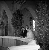 Vigsel i Säterbo kyrka. Brudparet herr Olsson och fröken Tallqvist knäböjer vid altarringen. Kyrkan är dekorerad med björkar.