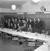 Avskedsfest för flygdirektör Nils Thorsson, Centrala Verkstaden Arboga
Bakre raden, från vänster: Nils Ekblom, okänd, Birger Haglund, Eilert Eiborn, Arne Norberg och Per Granström
Mellersta raden, från vänster: Ingvar Gustavsson, Jan Anders Källberg, Andrén (delvis skymd), Gunnar Seth, Folke Eriksson, okänd, okänd och Nils Lifvendahl
Sittande, från vänster: Nils Henriksson, Oskar Larsson, Bertil Henriksson, Nils Thorsson, Anders Högfeldt och Lars Harry Larsson
Borden är dukade med kaffekoppar och blombuketter i vaser. Nils har fått en present.
På väggen hänger en klocka.
CVA