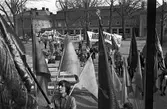 Demonstration på första maj. Demonstrationståget anländer till Olof Ahllöfs park. Människor bär plakat och banderoller.
Byggnaden i bakgrunden är Stadskällaren.