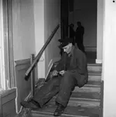 Reparationsarbete efter branden i televerkets lokal på Nygatan. En man sitter i en trappa och lagar ledningar. Han har arbetskläder och en keps med Televerkets märke på.