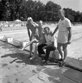 Jan-Urban Modigh (i kepsen), okänd flicka i baddräkt, Esbjörn Eriksson (badmästare) och Martin Sköld (vaktmästare på badet). Bakom dem ses utomhusbassängen.