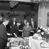 Elektrikerförbundets Arbogaavdelning har jubileumsfest. Män och kvinnor tar för sig vid gående bord. Blomsterdekorationer och ballonger.