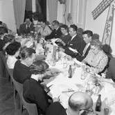 Elektrikerförbundets Arbogaavdelning jubilerar. Män och kvinnor vid dukat långbord. Måltiden är avslutad, nu börjar allsången. Framför dörren sitter Gustav Danielsson med hustru Signe (kvinnan med mörk klänning och halsband).