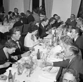Elektrikerförbundets Arbogaavdelning har jubileumsfest. Män och kvinnor sitter till bords och äter. Borden är dukade med blommor i vas och ljusstakar. Herman Skoglund (nästan mitt i bild) med näsduk i fickan. Snett mitt emot honom, ses profilen på Gustav Danielsson.