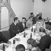 Elektrikerförbundets Arbogaavdelning har jubileumsfest. Festklädda män och kvinnor vid dukat bord. Måltiden är snart avslutad. En nejlika i vas, samt en ljusstake, är bordsdekorationer. Väggdekorationer.