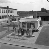 ESSO på Nygatan. Två män i overaller arbetar vid macken. Två kvinnor, med ESSO-mössor och banderoller håller i ballonger.
Bensinstationen har tre pumpar, en tvätthall och en smörjhall.
Byggnaden till vänster, med alla fönster, tillhör Engelbrektskolan.