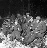 FBUl-ungdom övar i skogen. Grabbarna är klädda i yllerockar och mössor med öronlappar.
Pojkarna sitter på granris och äter ur sina plåtburkar. Det är vinter och snö.
Frivillig Befälsutbildning.