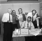 Folkpartiets valvaka på Arboga Tidnings redaktion. Eskil Östlund läser det senaste valresultatet på teleprinterremsan för chefredaktör John Wallstöm (sittande).
Stående, från vänster: Ulf Tillberg, Karl Waern, Eskil Östlund, Gösta Kvassman
Sittande: John Wallström
På skrivbordet står en räkneapparat och en radio. I bakgrunden skymtar en skrivmaskin.