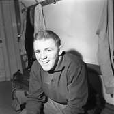 Roland Andersson deltar i fyrstadsbrottningen; Arboga - Eslöv - Uddevalla och Falkenberg
Porträtt av ung man som sitter på en bänk i omklädningsrummet