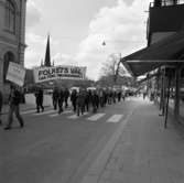 Första maj. Demonstration. Demonstrationståget går längs Nygatan. Människor bär banderoller och plakat.
I ledet ses Torbjörn Harlin och Nils Brodin.
Till vänster ligger Nikolaiskolan.
Socialdemokrater