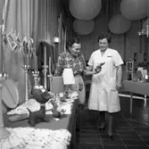 Försäljning hos pensionärerna på Strömsborg
Hantverk är uppställt på bordet. En personal, i vit arbetsrock, tittar på.