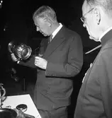 Konung Gustaf Vl Adolf är på Eriksgata. Här får han titta på silversamlingen i Heliga Trefaldighetskyrkan tillsammans med prosten E Olof Björsell.
För värdskapet, under kungens besök, svarade stadsfullmäktiges ordförande Jonas Carlsson och kommunalborgmästare Danliel Ekelund. Den organisationskommitté som ansvarade för arrangemangen, hade hos drätselkammaren begärt en summa av 3000 kronor för att täcka kostnaderna vid kungabesöket. Beloppet beviljades. 
Tiden för kungens besök var beräknad till 130 minuter.