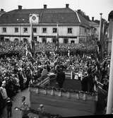 Konung Gustaf Vl Adolf på Eriksgata. Här talar han på Stora torget inför 6000 personer. På podiet, med ryggen mot fotografen, står Jonas Carlsson. De fyra män som står på rad, på podiet, är bortifrån: landshövding Ragnar Casparsson, landssekreterare Ludwig Lorichs, länsantikvarie Sven Drakenberg samt borgmästare Daniel Ekelund.
Framför estraden står en fotograf. Det är Bertil Forsén från tidningen Expressen. Intill honom står riksdagsman Iwar Andersson, polisman Axel Winblad och arrendator Sigfrid Silfverling på Koberg.
Till vänster om kungen ses Anna Hellberg och till höger Otto Åhlin. Otto hann få en pratstund med konungen.
För värdskapet svarade stadsfullmäktiges ordförande Jonas Carlsson och kommunalborgmästare Danliel Ekelund. Den organisationskommitté som ansvarade för arrangemangen, hade hos drätselkammaren begärt en summa av 3000 kronor för att täcka kostnaderna vid kungabesöket. Beloppet beviljades. 
Tiden för kungens besök var beräknad till 130 minuter.
En liknande bild, finns med i Reinhold Carlssons bok 