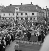 Människor trängs på Stora torget och Kapellgatan för att se och höra Kung Gustaf Vl Adolf. Han gästar Arboga under sin Eriksgata. I folkhavet kan urskiljas Frälsningsarmén och Hemvärnet.
På podiet står konungen. Jonas Carlsson står med ryggen mot fotografen. Fyra män, på rad, längst bak på scenen, bortifrån sett: landshövding Ragnar Casparsson, landssekreterare Ludwig Lorichs, länsantikvarie Sven Drakenberg samt borgmästare Daniel Ekelund.
För värdskapet svarade stadsfullmäktiges ordförande Jonas Carlsson och kommunalborgmästare Danliel Ekelund. Den organisationskommitté som ansvarade för arrangemangen, hade hos drätselkammaren begärt en summa av 3000 kronor för att täcka kostnaderna vid kungabesöket. Beloppet beviljades. 
Tiden för kungens besök var beräknad till 130 minuter.
En bild från detta tillfälle finns med i Reinhold Carlssons bok 