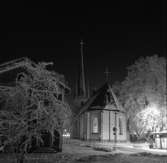 Heliga Trefaldighetskyrkan en stjärnklar vinterkväll.
Det lyser i kyrkan. Marken och träden är täckta av snö.