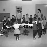 HSB´s barnträdgård. Två fröknar och alla barnen dansar runt en liten gran.
(HSB betyder Hyresgästernas sparkasse- och byggnadsförening)