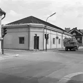 Korsningen Hamngatan - Herrgårdsgatan. Huset renoveras på insidan, en hantverkare syns i fönstret. På Östra Hamngatan kör en lastbil från Albin Rapps Konfektionsfabrik. Den är lastad med säckar.