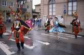 Arbogakarnevalen pågår. Paraden har nått fram till Hökenbergs gränd. Uppklädda dansare i regnet.
I hörnet, i lika dana regnjackor, står Lotta Winkler Yngve och Olof Yngve. I bakgrunden, till vänster, ses Sandbergs herrekiperingen på Nygatan.