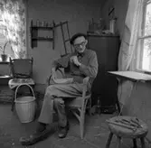 Korgmakare Oskar Larsson i Sjölunda, Tyringe.
Oskar har sin verkstad i ett av rummen i bostadshuset. På väggen hänger en såg. En färdig korg står på golvet. På byrån ligger en borr. På pallen ligger ett par tänger och en hammare.
Det står krukväxter i fönstret.
Oskar är gift med Maja.
Oskar lärde grannbarnen att spela schack.